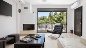Ein modernes Wohnzimmer mit Flachbildfernseher, Couchtisch mit einem Buch, schwarzem Ledersessel und einer Glastür zum Außenbereich.