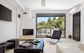 Uma sala de estar moderna com televisão de tela plana, mesa de centro com um livro, poltrona de couro preto e porta de vidro deslizante para área externa.