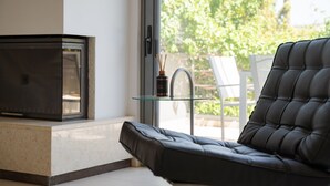Ein modernes Wohnzimmer mit Sofa, Glastisch, Kamin und Blick auf Grünflächen.