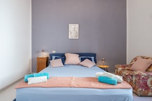 Un dormitorio con cama, almohadas, mesita de noche y una silla, además de una obra de arte colgada en la pared.