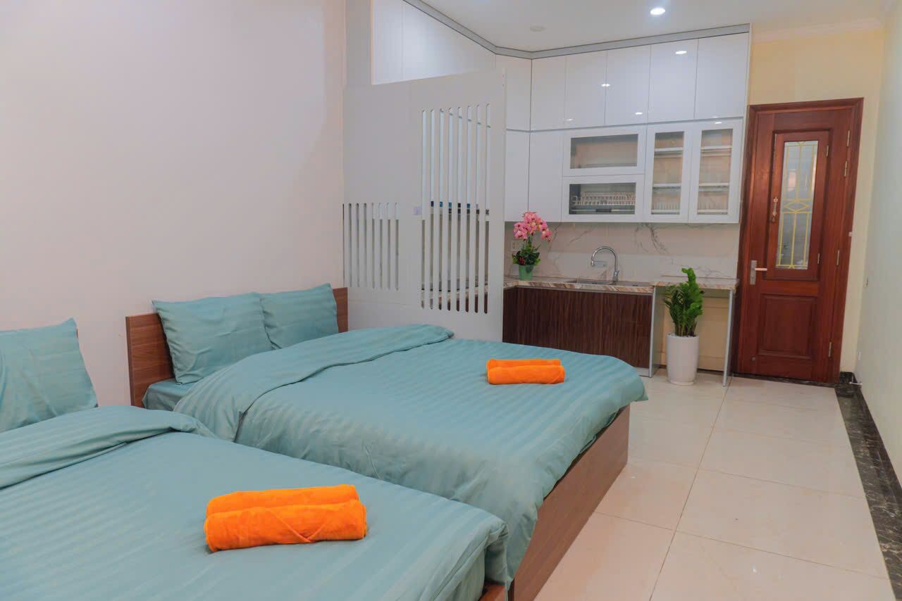 A bedroom with two beds, a small kitchenette, and a wooden door.
