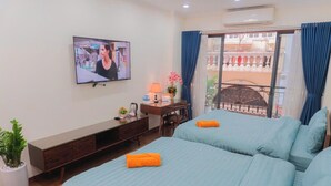Quarto de hotel com duas camas, televisão, escrivaninha com luminária, planta em vaso e vista para o exterior.