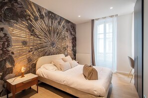 A bedroom with a large bed, a nightstand with a lamp, a wall mural, and a window with curtains. - ✨ Elegance & comfort in the heart of Annecy ✨ (Annecy)