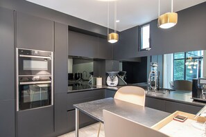 A modern kitchen with a built-in oven, a dining area with a table and chairs, and pendant lighting. - ✨ Elegance & comfort in the heart of Annecy ✨ (Annecy)