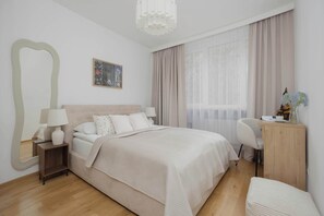Ein Schlafzimmer mit Bett, Nachttisch, Lampe, Stuhl, Schreibtisch und einem großen Spiegel.