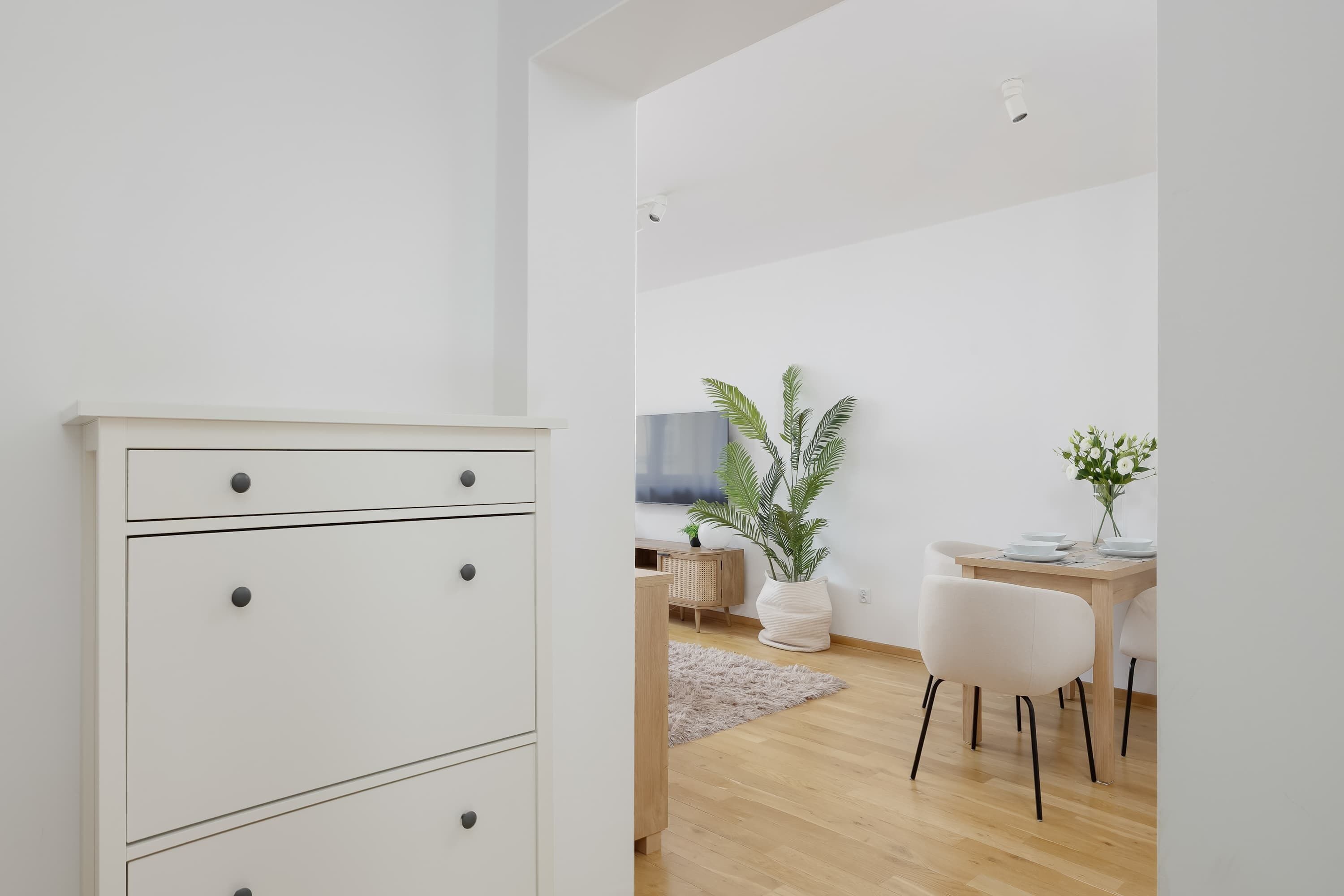 A modern, minimalist room with a white dresser, a wooden dining table, and a potted plant.