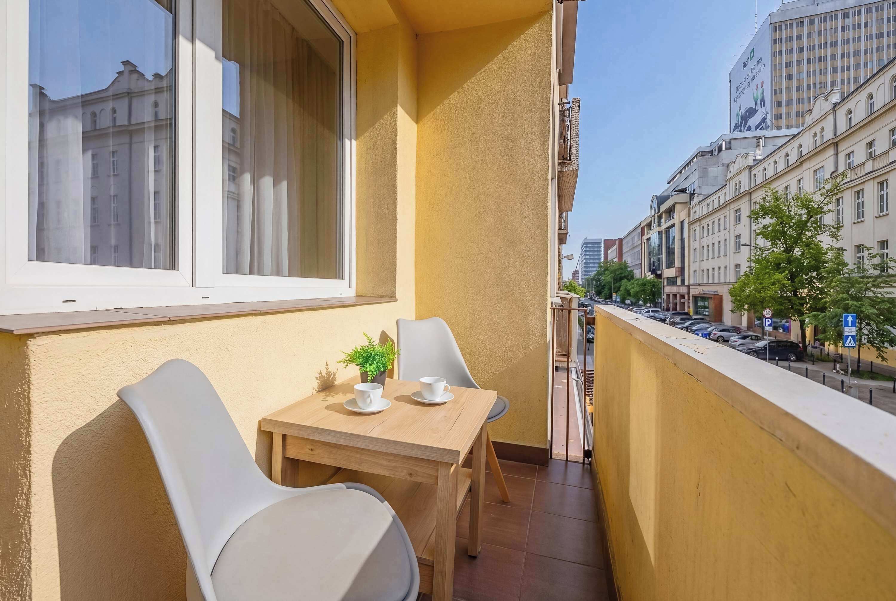 A balcony with a table and chairs, a potted plant, and a view of city buildings.