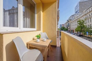 Ein Balkon mit Tisch und Stühlen, einem Blumentopf und Blick auf Stadtgebäude.