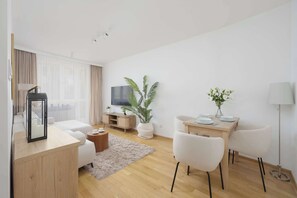 Ein modernes Wohnzimmer mit Sofa, Couchtisch, Fernseher, Esstisch mit Stühlen und einer Topfpflanze.