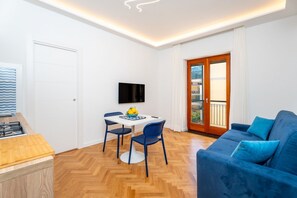 Ein kompakter Wohnbereich mit Küchenzeile, Essbereich, Sofa und Fernseher.
