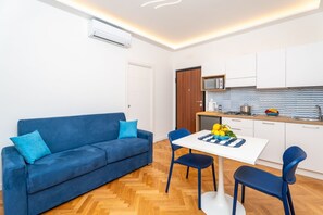 Ein kompakter Wohnbereich mit Sofa, Esstisch, Stühlen, einer Küchenzeile und einer Tür.