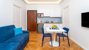 A compact living space with a sofa, dining table, chairs, kitchenette, and a TV mounted on the wall. - Nicea Apartment - Sorrento center (Sorrento)