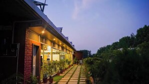 A building with a covered walkway, potted plants, and a view of a hill. - Abha Farms And Resort (Udaipur)