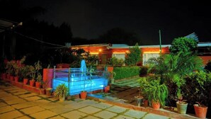 A courtyard with a fountain, potted plants, and a building with a blue roof. - Abha Farms And Resort (Udaipur)
