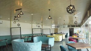 A spacious indoor area with seating arrangements, pendant lighting, and a visible kitchen area. - Abha Farms And Resort (Udaipur)