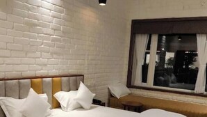 A neatly made bed with white bedding, a wooden headboard, and a window with curtains. - Abha Farms And Resort (Udaipur)