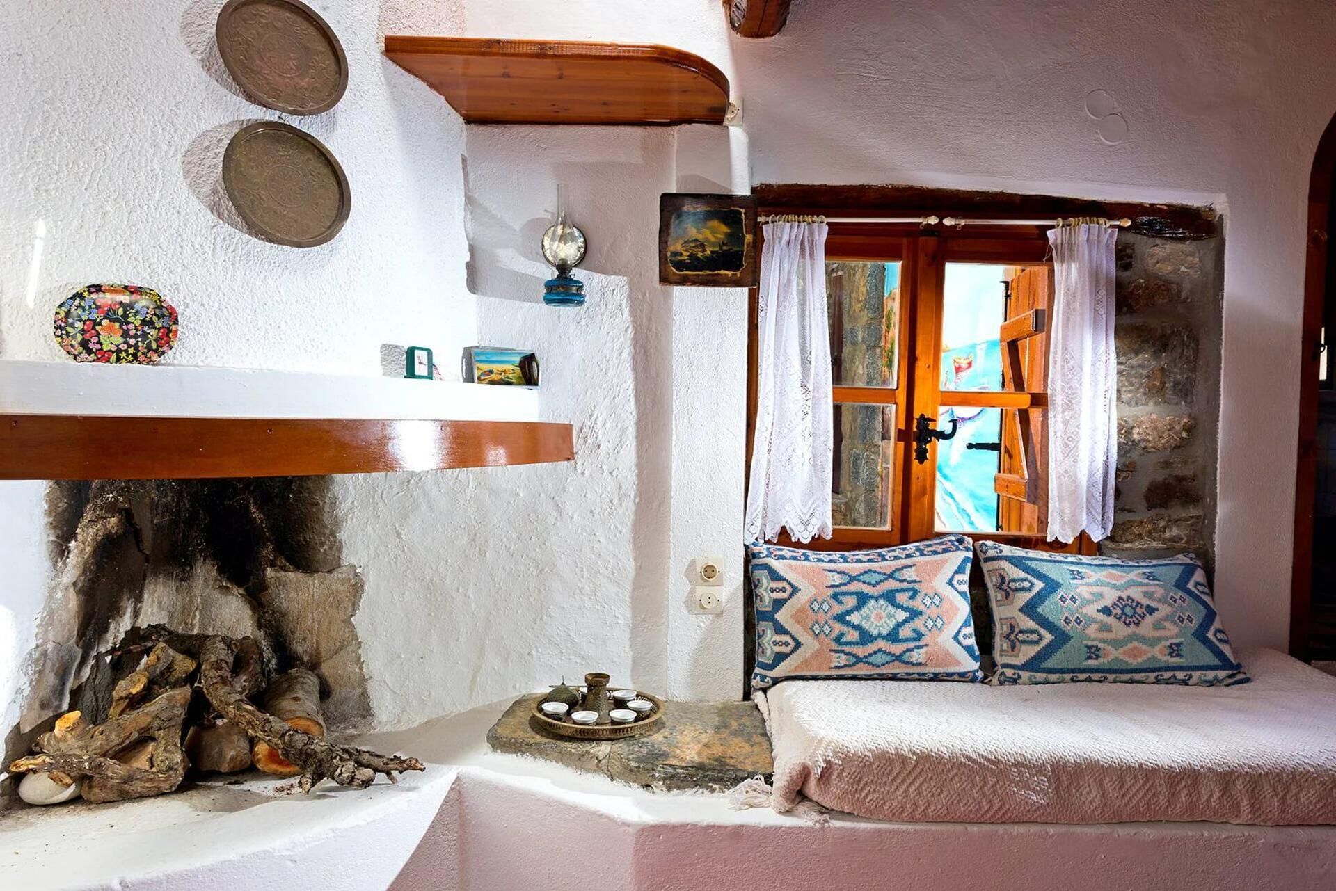Une pièce chaleureuse avec une cheminée, une fenêtre avec des rideaux et une petite table agrémentée d’objets décoratifs.