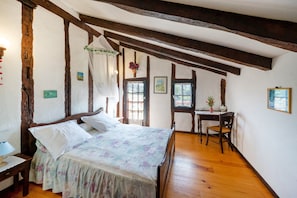 A bedroom with a wooden ceiling, a bed with floral bedding, a desk, and a chair. - Otsanda Logelak Guest Rooms – Renovated Basque Farmhouse with Mountain Views (Sare)