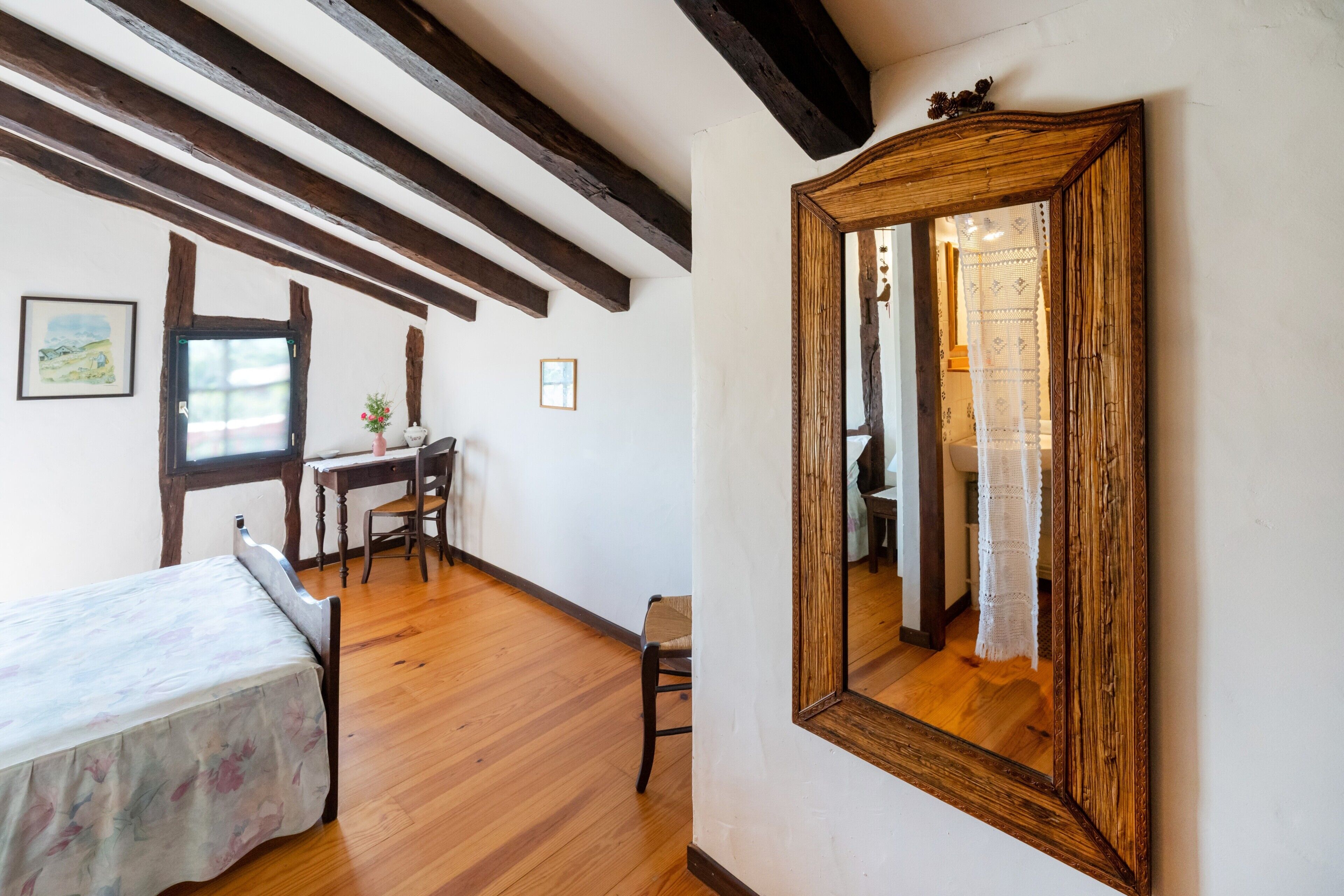 A room with wooden beams, a bed, a desk, a chair, and a large mirror.