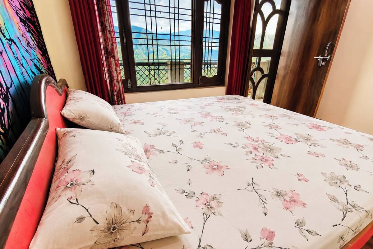 A bed with floral bedding, a view of mountains through a window, and a red curtain.