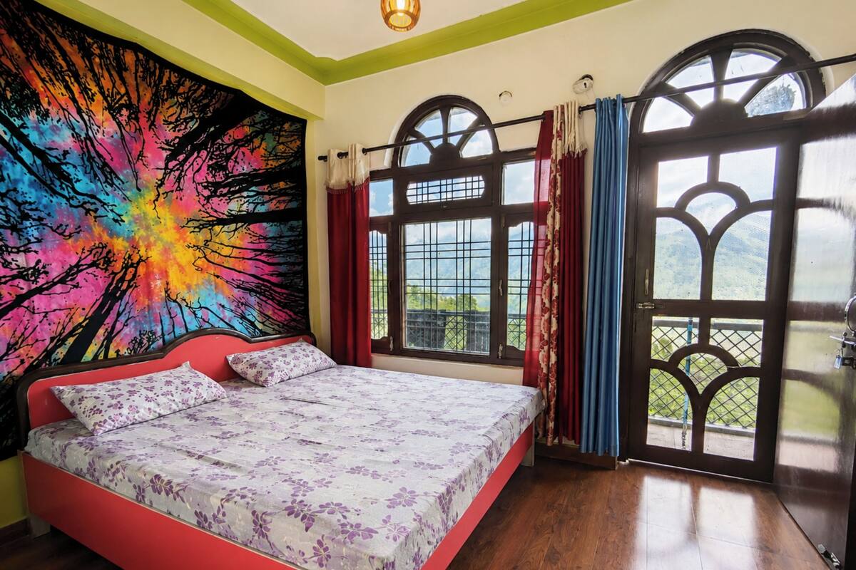A bedroom with a bed, a colorful tapestry, and large windows with curtains.