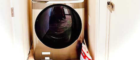 Une buanderie équipée de deux machines à laver à chargement frontal superposées, d’un miroir et d’un sac à linge.