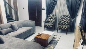 A living room with a grey sofa, a wooden coffee table, and patterned armchairs. - Binga14 Luxury Apartment (Lagos)