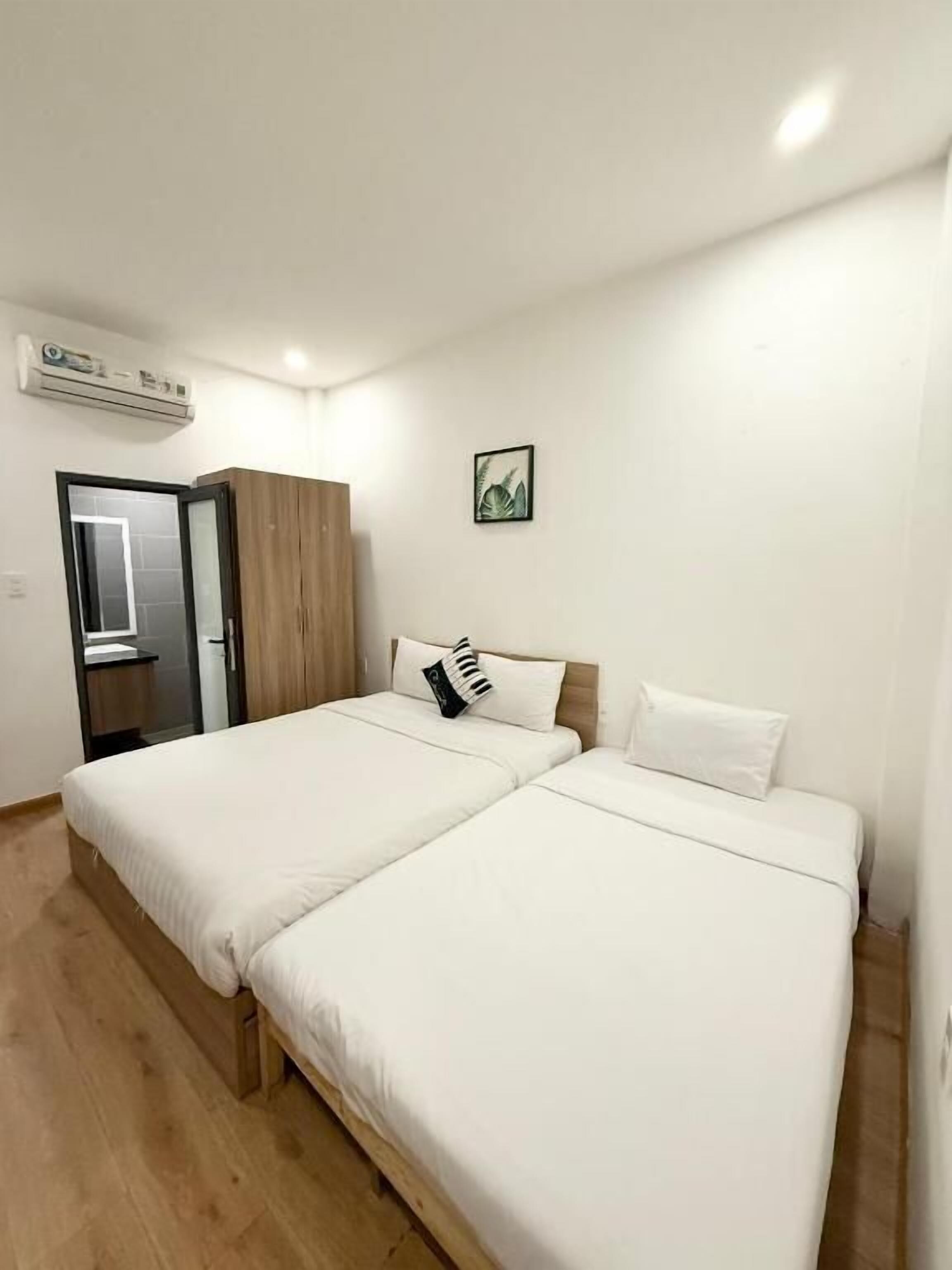 A room with two beds, a wardrobe, an air conditioning unit, and a framed picture on the wall.