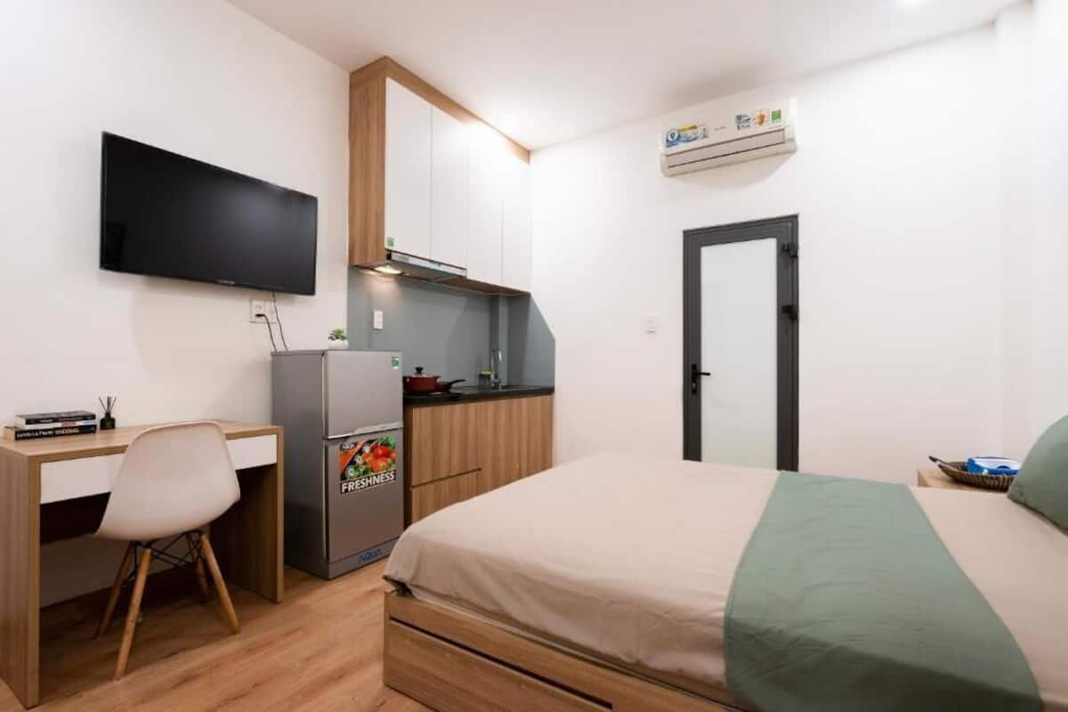 Ein Schlafzimmer mit Bett, Schreibtisch, Stuhl, Fernseher, einer Küchenzeile und einer Klimaanlage.