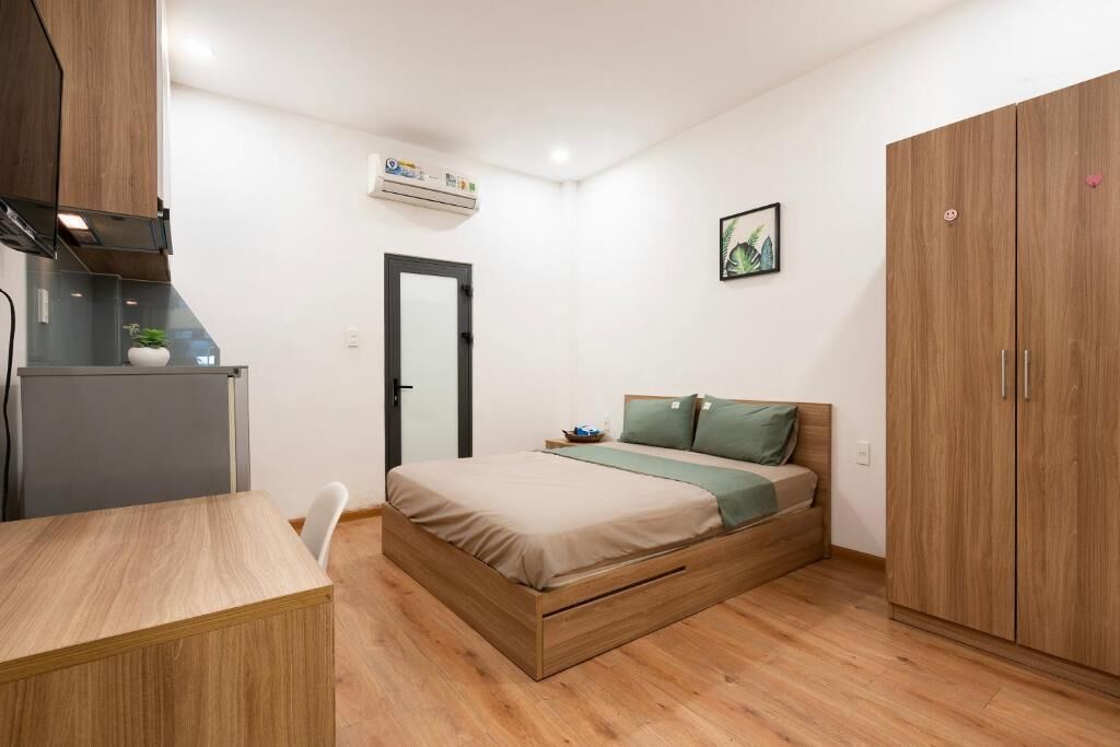 A bedroom with a bed, a desk, a wardrobe, and an air conditioning unit.