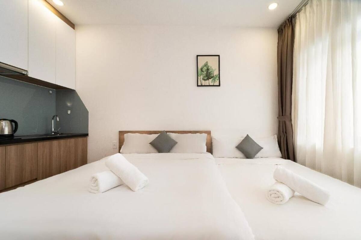 Ein Hotelzimmer mit Bett, einer kleinen Küchenzeile, einem gerahmten Bild an der Wand und einem Fenster mit Vorhängen.