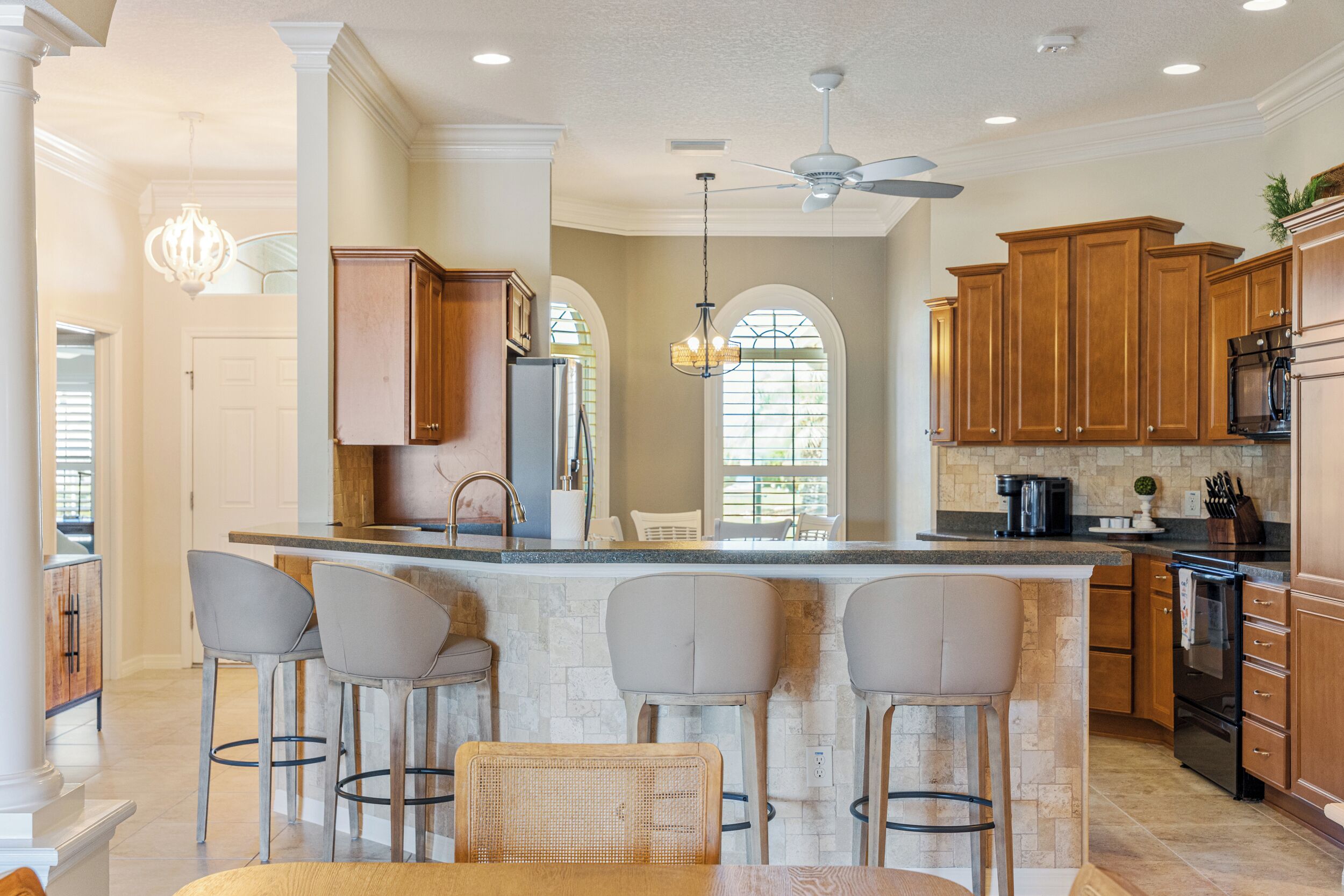 A kitchen with a bar area, wooden cabinets, a ceiling fan, and a stone backsplash.