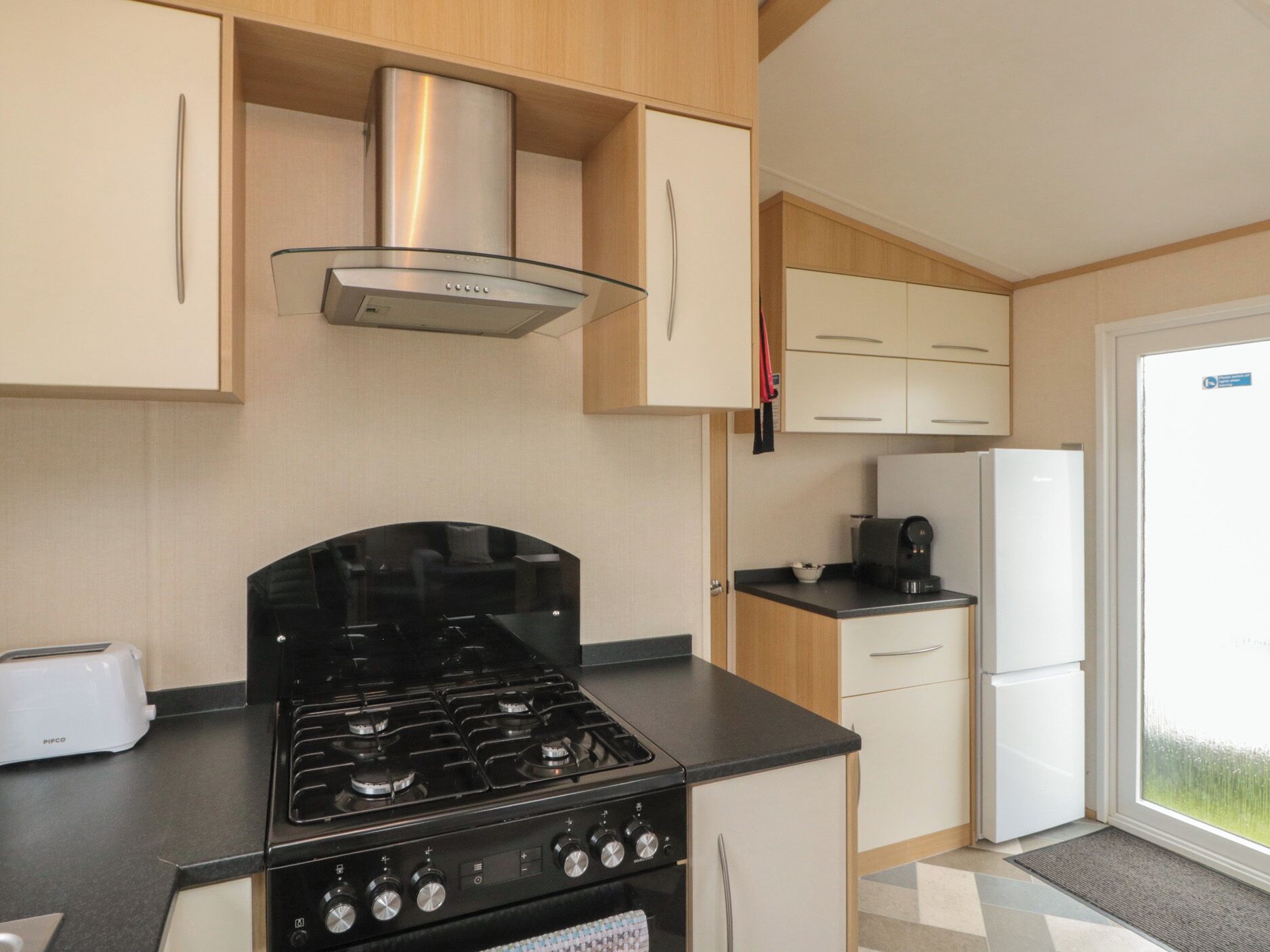 A compact kitchen with a gas stove, a coffee maker, and a refrigerator.
