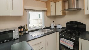 A compact kitchen with a microwave, stove, sink, and cabinets. - 21 Dunlin Dell (Bridlington)