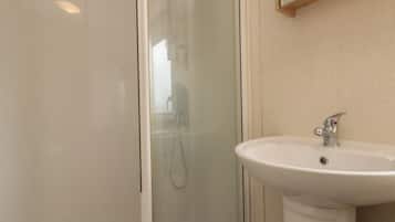 Casa de banho com cabine de duche em vidro, lavatório branco e espelho sobre o lavatório.
