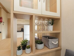 Una cocina con armarios blancos, un refrigerador y una repisa con cristalería y plantas.
