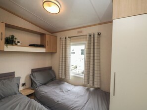 Un dormitorio compacto con cama, mesita de noche, estante con plantas y ventana con cortinas.