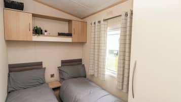 Un dormitorio pequeño con dos camas, una estantería con plantas y una ventana con cortinas.