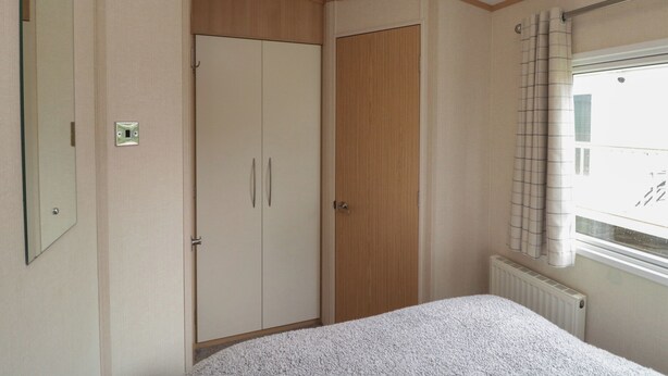 A bedroom with a bed, a wardrobe, a radiator, and a window with curtains. - 21 Dunlin Dell (Bridlington)