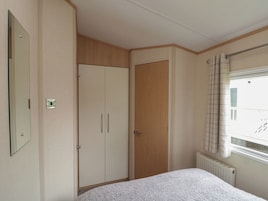 Quarto com cama, guarda-roupa, radiador e janela com cortinas.