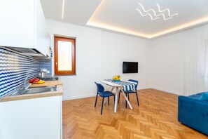 A modern kitchen with a built-in stove, a dining area with a table and chairs, and a blue sofa in a bright room with wooden flooring. - Nerea Apartment | Sea View Balcony (Sorrento)