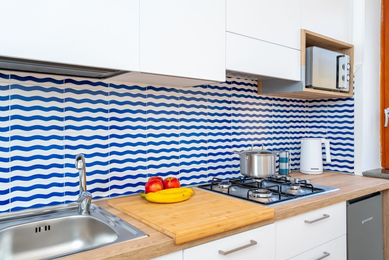 Una cocina de diseño moderno, con un lavamanos de acero inoxidable, una tabla de cortar con frutas, una estufa a gas y un microondas.