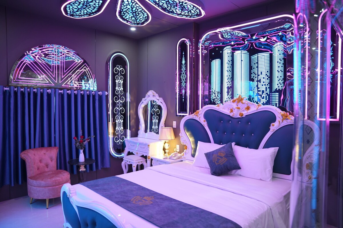 A bedroom with a large bed, a vanity with a mirror, and a chair.
