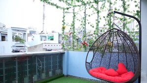 A rooftop garden with artificial grass, a hanging red cushioned chair, and a view of buildings. - Haven Hotel (Ho Chi Minh City)