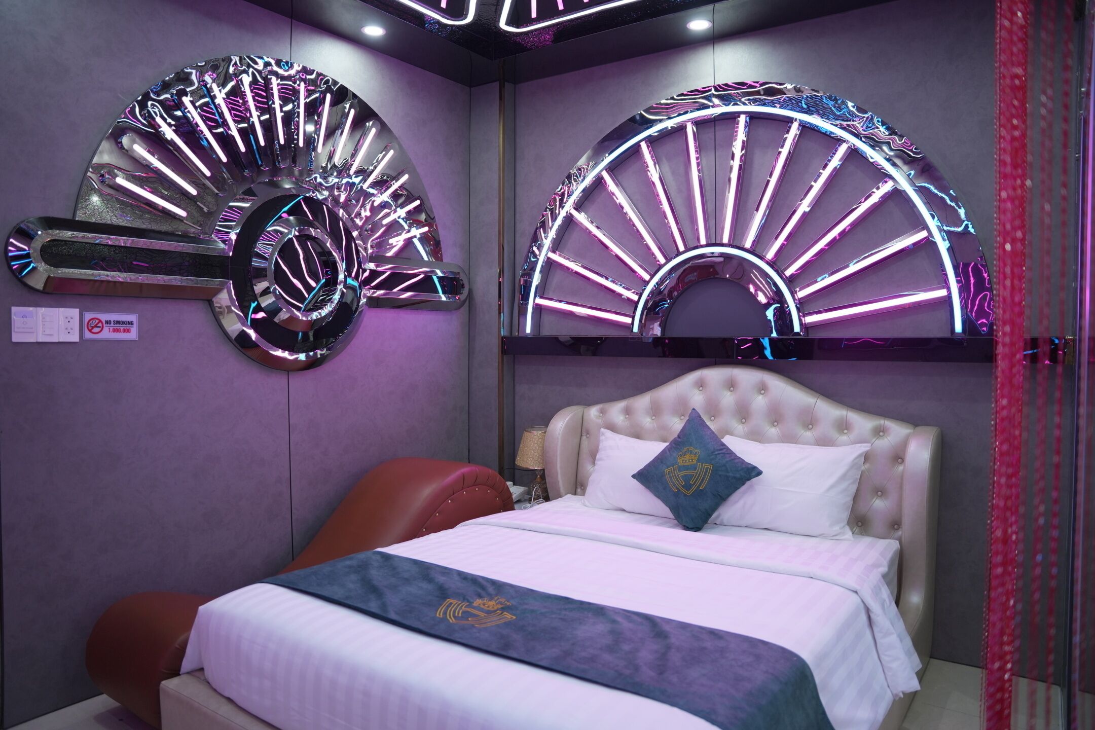 A bedroom with a bed, a headboard, a wall-mounted fan, and a neon light design.