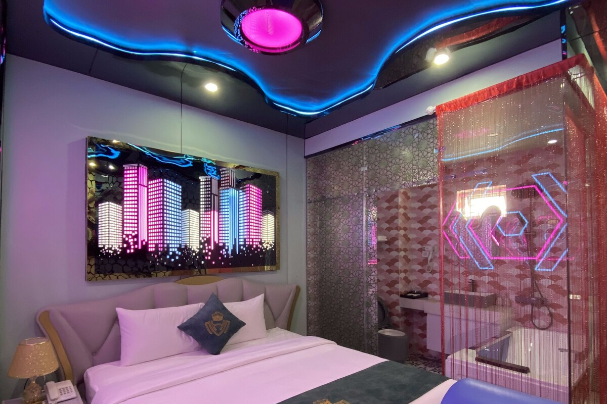 A modern bedroom with a bed, a nightstand, a wall-mounted TV, and a bathroom with a shower area.