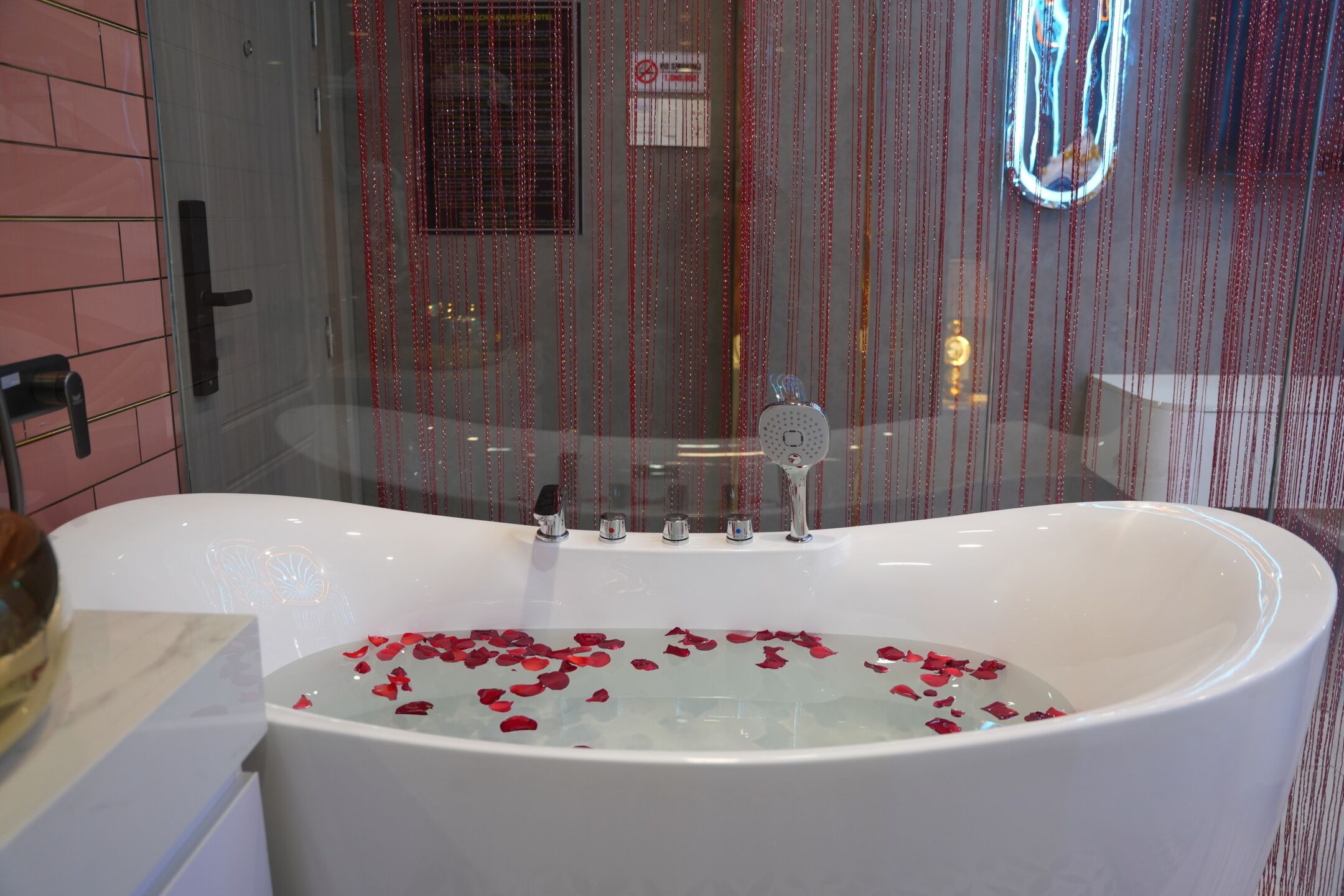 Eine Badewanne mit Rosenblüten, eine Glasdusche und eine geflieste Wand.