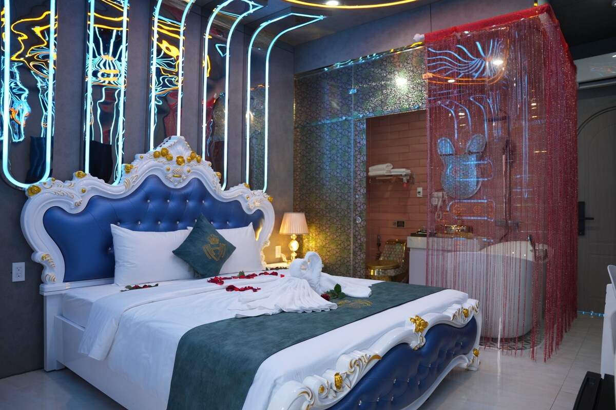 A bedroom with a large bed, a mirror, a vanity, and a shower area.