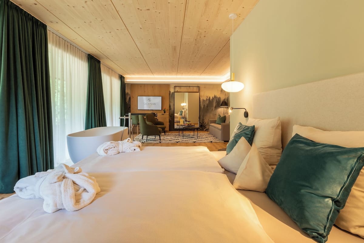 A hotel room with a large bed, a sitting area with a sofa and armchairs, a wooden ceiling, and a television on the wall.