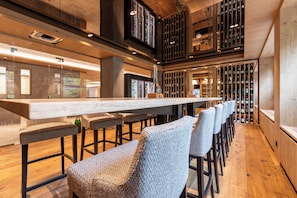 A bar area with a long counter, multiple bar stools, and wine racks in the background. - Sackmann Design Genuss & SPA Resort (Baiersbronn)